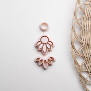 May include: Three pink plastic cookie cutters in the shape of a flower, a circle, and a row of leaves.