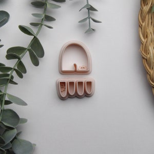 May include: A pink plastic cookie cutter shaped like a pair of trousers with a top and bottom piece. The top piece is a curved shape and the bottom piece has four legs.
