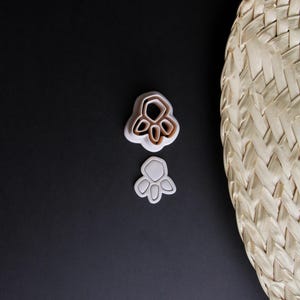 Könnte beinhalten: Zwei weiße Plastik-Ausstecher in Form einer Pfote. Der größere Ausstecher hat ein detailliertes Design mit mehreren Schichten. Der kleinere Ausstecher ist eine einfache Umrandung einer Pfote.