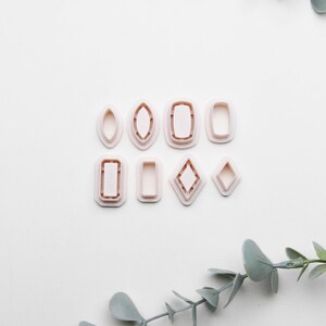 May include: A set of ten plastic cookie cutters shaped like different gemstones. The cutters are white and arranged in two rows on a white background.