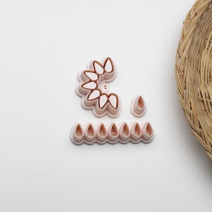 May include: A selection of pink plastic petal-shaped cookie cutters. The cutters are arranged in a variety of shapes, including a half-circle, individual teardrops, and a row of teardrops. A woven basket is in the background.
