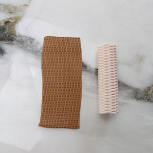May include: Two pieces of craft material are displayed against a marble background. One is a rectangular, woven brown piece. The other is a cylindrical, woven off-white piece. The textures of both pieces are visible.