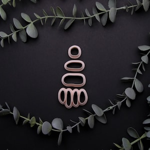 May include: A set of five pink metal cookie cutters shaped like a Christmas tree. The cutters are arranged in a stack, with the largest cutter at the bottom and the smallest cutter at the top. The cutters are on a black background.