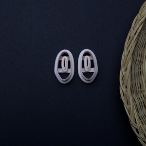 May include: Two oval-shaped, light pink, plastic earring posts with a small, round, white, plastic insert in the center.