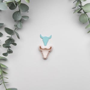 Peut inclure: Un ensemble de deux emporte-pièces en forme de tête de taureau. Le plus grand emporte-pièce est de couleur rose clair et le plus petit est de couleur bleu clair.