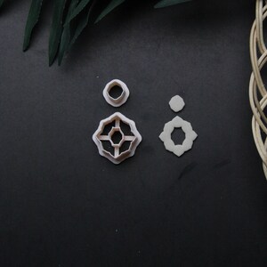 May include: Three white plastic cookie cutters on a black background. The cutters are shaped like a circle, a flower, and a star.