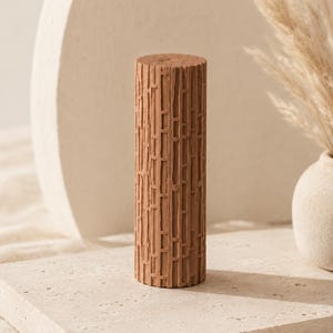 May include: A cylindrical terracotta-colored object featuring a textured surface with a repeating pattern of vertical and horizontal raised lines. The object has a flat top and bottom, with a matte finish and a consistent earthy brown tone throughout.