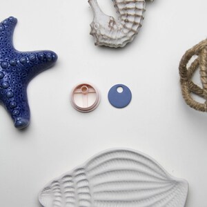 May include: A selection of nautical decorations. The image shows a blue starfish, a seahorse, a seashell, a rope knot, a pink circle, and a blue tag. All items are on a white surface.