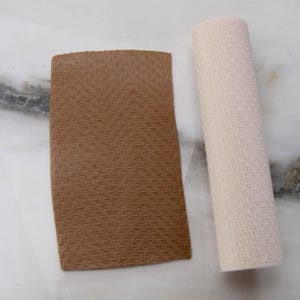 May include: A brown, rectangular, textured pad and a rolled, off-white, textured cylinder are displayed on a white surface. The pad has a woven pattern, and the cylinder appears to be made of a similar material.