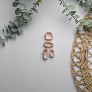 May include: A set of four pink plastic cookie cutters shaped like a person. The cutters are arranged in a vertical stack, with the head cutter on top and the feet cutters on the bottom.