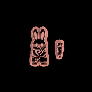 May include: A pink plastic cookie cutter set featuring a bunny holding a carrot and a separate carrot-shaped cutter. The bunny is wearing overalls and has detailed facial features. Ideal for Easter-themed baking.