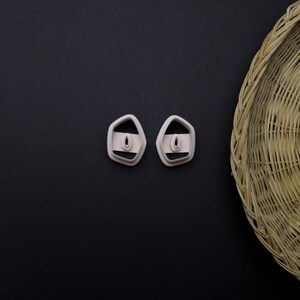May include: Two white plastic cookie cutters shaped like a rounded rectangle with a small oval cutout in the center. The cutters are on a black background.