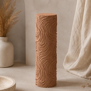 May include: A cylindrical terracotta-coloured roller featuring a deeply embossed, swirling, wave-like texture across its entire surface. The tool has a flat circular top and bottom, designed with a continuous pattern for creating impressions in clay or dough.