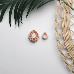 May include: Two pink plastic cookie cutters, one shaped like a teardrop with a scalloped edge and the other a simple teardrop shape.