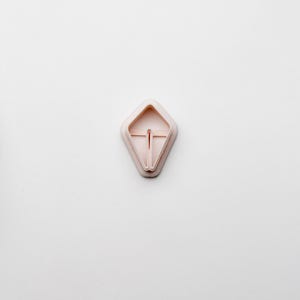 May include: A pink plastic cookie cutter shaped like a diamond with a small opening in the centre.
