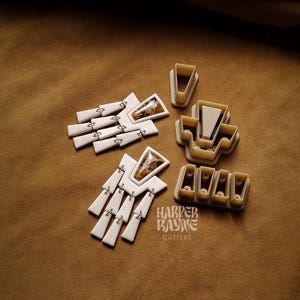 May include: A collection of beige and brown cookie cutters in various shapes, including geometric and rectangular designs. Some cutters feature decorative inlays. The text "HARPER KAYNE CUTTERS" is visible.