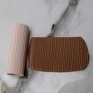 May include: Two polymer clay tools with a textured pattern. One is a light pink cylinder, and the other is a brown rectangular shape. Both have a repeating chevron design, ideal for adding texture to clay projects.