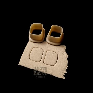 May include: Two beige plastic cookie cutters shaped like squares. The cutters are on top of a beige piece of paper with the text "HARPER BAYNE CUTTERS" printed on it.