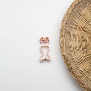 May include: Two white plastic cookie cutters shaped like a mermaid tail and a seashell top. The cutters are on a white surface.