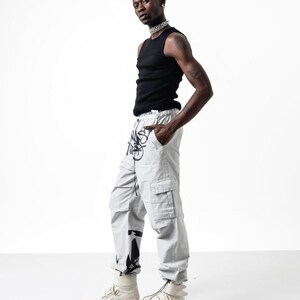 May include: A person wearing a black tank top, light gray cargo pants with black graphic print, and white high-top sneakers.