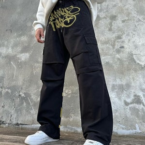 May include: Black cargo pants with a gold graphic print. The print features the words "Mind The Gap".