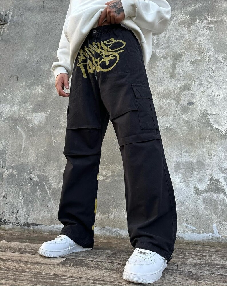 May include: Black cargo pants with a gold graphic print. The print features the words "Mind The Gap".