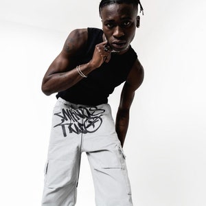 May include: A person wearing a black tank top and light gray cargo pants with black graffiti-style text that says "Worlds Trade".