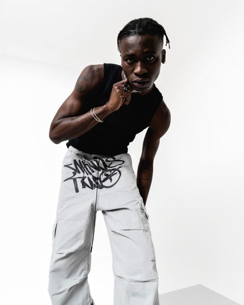 May include: A person wearing a black tank top and light gray cargo pants with black graffiti-style text that says "Worlds Trade".