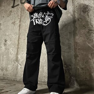 May include: Black cargo pants with a white graphic print that says "SMALL TRIBE" on the front.