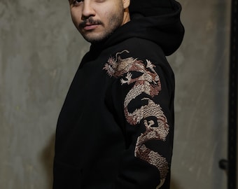 May include: A black hoodie with a large embroidered dragon design on the left sleeve. The dragon is a light brown and gold colour.