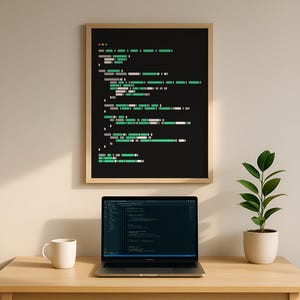 May include: A framed print with a black background and green and white code-like design hangs above a laptop on a wooden desk. A white mug and potted plant are also on the desk. The laptop screen displays code.