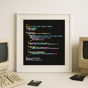 Puede incluir: Una impresión enmarcada con código colorido sobre un fondo negro. El código se compone de líneas y formas de varios colores. La impresión se muestra sobre una superficie blanca con un ordenador vintage, un teclado y un disquete.