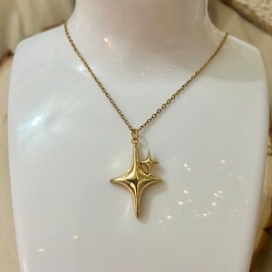 May include: A gold necklace with a star-shaped pendant. The pendant has a smaller star on top of it.