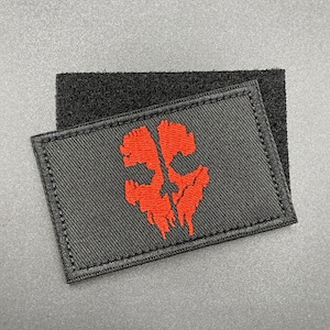 May include: Black patch with red embroidered skull design. The patch has a hook and loop backing.