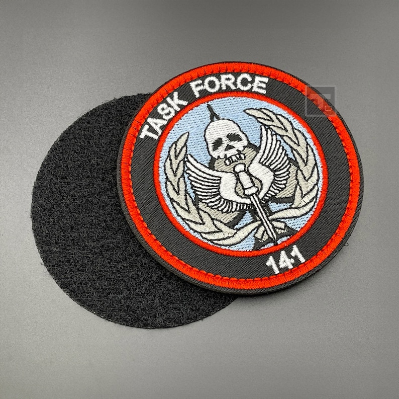 May include: A black and red embroidered patch with a skull and crossbones design. The patch says "Task Force 141" and has a white background with a blue sky.