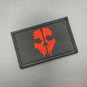 May include: A black patch with a red embroidered skull design. The skull is stylized and has a dripping effect.