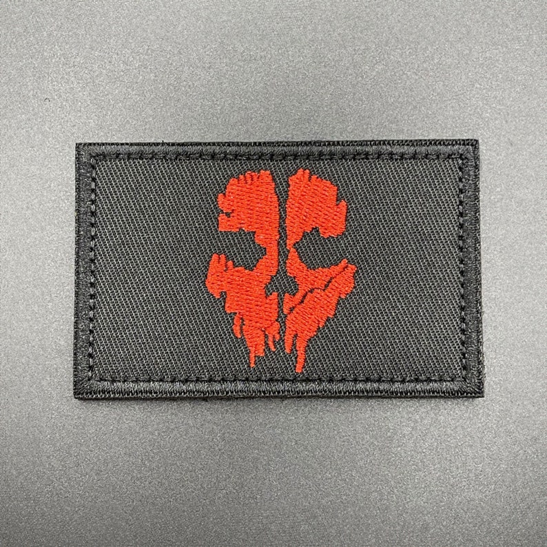 May include: Black embroidered patch featuring a red skull design. The skull is stylised and has a dripping effect.