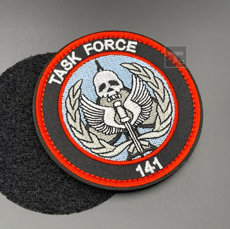 May include: A black and red embroidered patch with a skull and crossbones design. The patch says "Task Force 141" in white lettering.