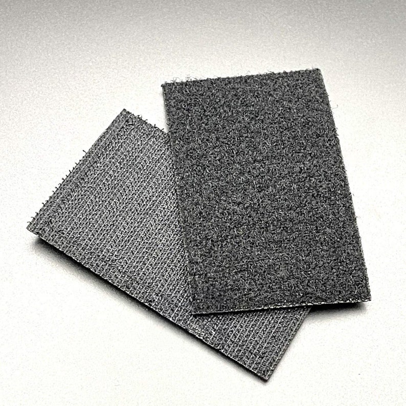 May include: Two pieces of black hook and loop fastener, also known as Velcro. The larger piece is on top of the smaller piece.