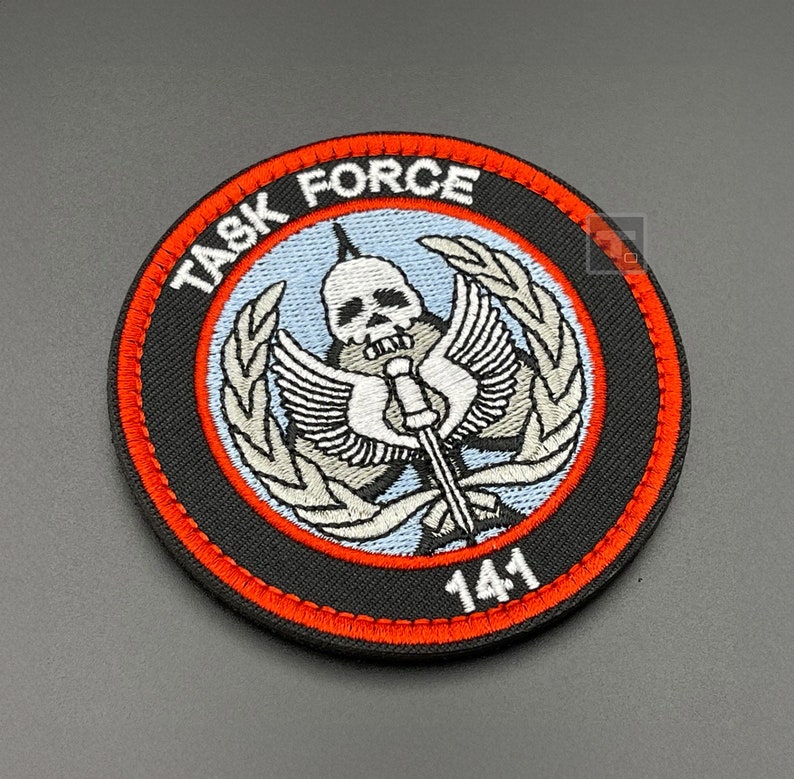 May include: A black and orange embroidered patch with a skull and crossbones design. The text "TASK FORCE 141" is embroidered around the skull.