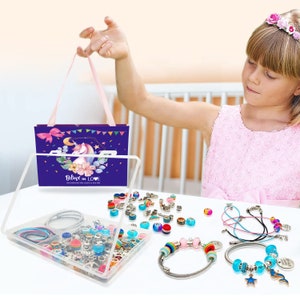 May include: A clear plastic storage box filled with colorful beads, charms, and elastic cords. The box is open and the contents are visible. There are two bracelets made with the beads and charms. The box is sitting on a white table. The box has a purple and blue unicorn design on the side with the text "Believe in Love".