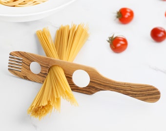May include: A wooden pasta server with two holes for holding spaghetti. The server is made of olive wood and has a natural wood grain. A bundle of spaghetti is resting on the server.
