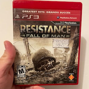 May include: A red PlayStation 3 game case for the game Resistance: Fall of Man. The case has a mature rating and features a skull with a helmet on the front.