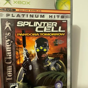 Op de afbeelding: Xbox-gamecase voor Splinter Cell: Pandora Tomorrow, met een personage dat een pistool vasthoudt voor een tropische achtergrond. De game is door de ESRB met T voor tieners beoordeeld.