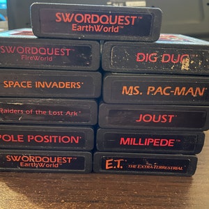 Op de afbeelding: Een stapel van tien vintage Atari-spelcartridges, waaronder Swordquest: EarthWorld, Swordquest: FireWorld, Dig Dug, Space Invaders, Raiders of the Lost Ark, Pole Position, Ms. Pac-Man, Joust, Millipede en E.T. de buitenaardse.