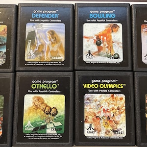 May include: Eight Atari game cartridges, each with a different game title and artwork. The cartridges are black with white text and graphics. The games include Outlaw, Defender, Bowling, Golf, Berzerk, Othello, Video Olympics, and Casino.
