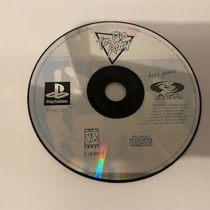 May include: A silver PlayStation game disc for Ten Pin Alley, a head games title. The disc has a silver background with a black centre and a blue PlayStation logo. The text "Ten Pin Alley" is in a white font with a black outline. The text "head games" is in a black font. The text "SLUS-00377" is in a white font. The text "COMPACT DISC" is in a black font.