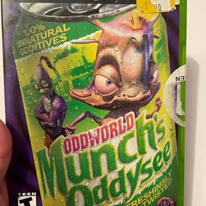 May include: A green and yellow video game case for Xbox with the title "Oddworld: Munch's Oddysee" and a cartoon image of a green, purple, and brown creature. The case is labeled "100% Unnatural Additives" and "Refreshingly Twisted".
