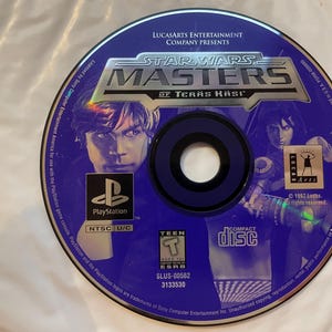 Puede incluir: Un disco de juego de PlayStation azul para "Star Wars: Masters of Teras Kasi". El disco presenta imágenes de personajes del juego, el logotipo de PlayStation y la clasificación ESRB Teen. El disco es un disco compacto.