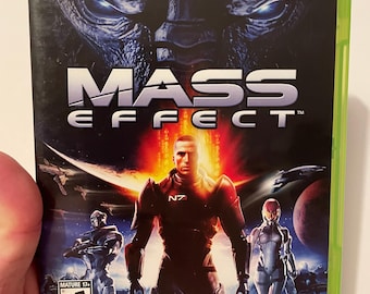 May include: Mass Effect Xbox 360 game case. The cover features a central figure in armor with a red and orange background, and the game's title in large white letters. The Xbox 360 logo and "Only on Xbox 360" are at the top.